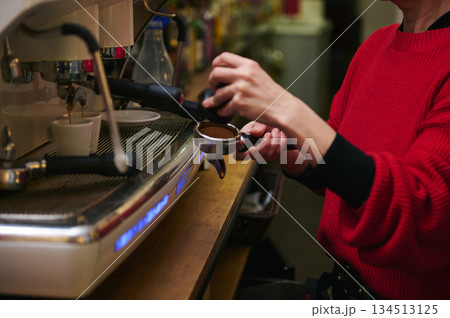 A Hispanic middle-aged cafe worker operates a professional espresso machine, preparing a shot for customers. Warm red sweater, bustling counter, focus on craft, hospitality, and small-business cafe A Hispanic middle-aged cafe worker operates a professional espresso machine, preparing a shot for customers. Warm red sweater, bustling counter, focus on craft, hospitality, and small-business cafe 134513125