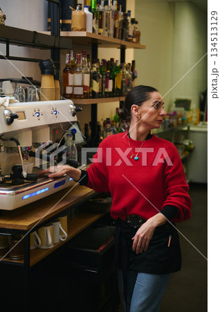A Hispanic cafe owner in a red sweater works at an espresso machine in a cozy cafe, with shelves of bottles behind her, projecting hospitality and small business vibes. A Hispanic cafe owner in a red sweater works at an espresso machine in a cozy cafe, with shelves of bottles behind her, projecting hospitality and small business vibes. 134513129