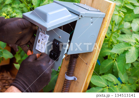 Worker installs electrical outlet in garden to enhance power access for tools equipment Worker installs electrical outlet in garden to enhance power access for tools equipment 134513141