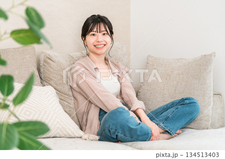 自宅のリビングのソファーでくつろぐ笑顔の若いアジア人女性 自宅のリビングのソファーでくつろぐ笑顔の若いアジア人女性 134513403