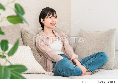 自宅のリビングのソファーでくつろぐ笑顔の若いアジア人女性 134513404