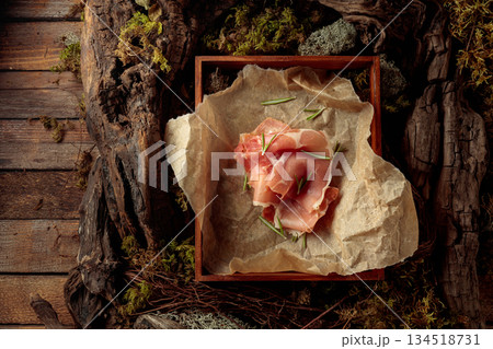 Prosciutto with rosemary on a paper in wooden box. Prosciutto with rosemary on a paper in wooden box. 134518731