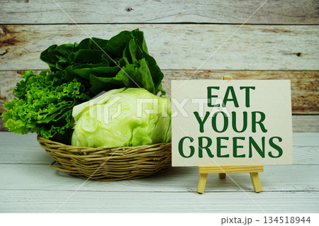 "Eat Your Greens" message on a small easel next to a basket of fresh green leafy vegetables 134518944