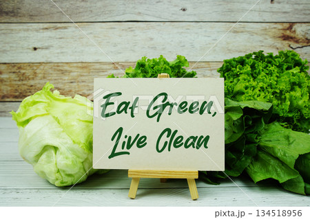 "Eat Green, Live Clean" message on a small easel next to a basket of fresh green leafy vegetables "Eat Green, Live Clean" message on a small easel next to a basket of fresh green leafy vegetables 134518956