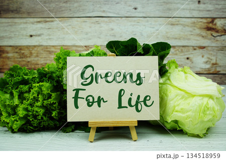 "Greens For Life" message on a small easel next to a basket of fresh green leafy vegetables 134518959