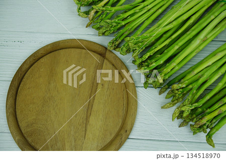 Bunch of fresh green asparagus stems with cutting wooden board on wooden background Bunch of fresh green asparagus stems with cutting wooden board on wooden background 134518970