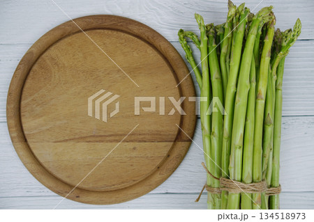 Bunch of fresh green asparagus stems with cutting wooden board on wooden background 134518973
