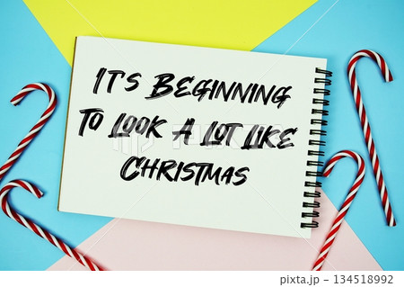 It's Beginning To Look A Lot Like Christmas message of season holidays written on notepad with candy cane decoration on pastel background It's Beginning To Look A Lot Like Christmas message of season holidays written on notepad with candy cane decoration on pastel background 134518992