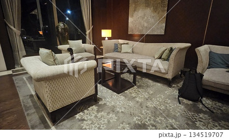 An elegant lounge with beige armchairs, floral rugs, and warm lighting offers a refined, tranquil space enriched by art, symmetry, and a metallic dragonfly sculpture casting a graceful shadow An elegant lounge with beige armchairs, floral rugs, and warm lighting offers a refined, tranquil space enriched by art, symmetry, and a metallic dragonfly sculpture casting a graceful shadow 134519707