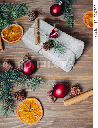 A Christmas gift lies on a wooden table, next to it there are dried oranges, cinnamon shelves, pine cones, a fir branch as a symbol of Christmas 134520705