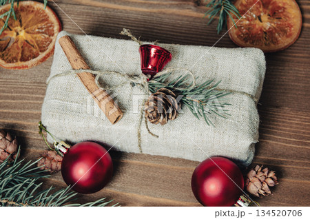 A Christmas gift lies on a wooden table, next to it there are dried oranges, cinnamon shelves, pine cones, a fir branch as a symbol of Christmas 134520706