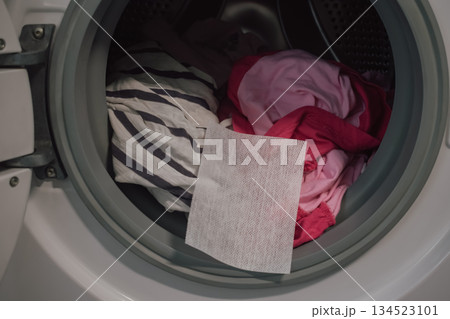 open washing machine full of colorful clothes with color catcher sheet for laundry protection 134523101