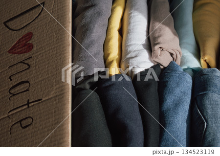 Box of neatly folded clothes ready for donation at home, highlighting generosity and community spirit on a sunny day 134523119