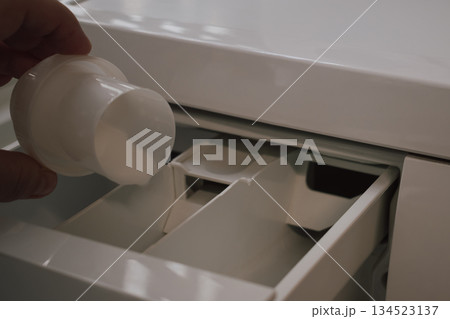 woman's hand pouring liquid fabric softener from measuring cup into washing machine dispenser woman's hand pouring liquid fabric softener from measuring cup into washing machine dispenser 134523137
