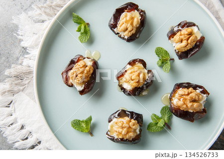 Delicious dates generously stuffed with cream cheese, walnuts and honey in a porcelain plate closeup. Horizontal top view 134526733