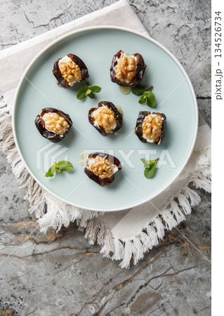 Arabic stuffed dates with cream cheese, walnuts and honey close-up in a plate. Vertical top view Arabic stuffed dates with cream cheese, walnuts and honey close-up in a plate. Vertical top view 134526734