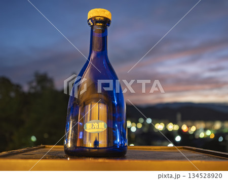夕暮れの空と夜景に佇む青い日本酒 134528920