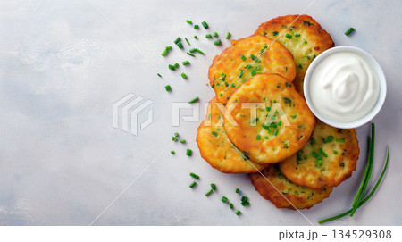 Golden potato pancakes with chopped herbs served with sour cream on a light textured background 134529308