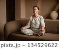 Woman meditate on sofa in minimalist beige room 134529622