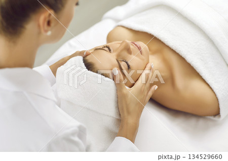 Close up masseur hands making face relaxing massage to a young girl in beauty salon. 134529660