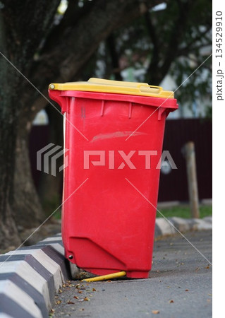 Red outdoor trash bin with a yellow lid placed on a roadside curb in an urban environment Red outdoor trash bin with a yellow lid placed on a roadside curb in an urban environment 134529910