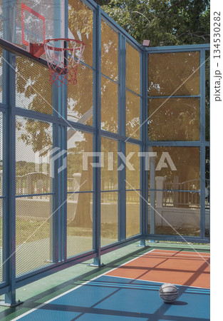 Midday shadows fall across an old basketball resting on the outdoor basketball court in the city park. Midday shadows fall across an old basketball resting on the outdoor basketball court in the city park. 134530282