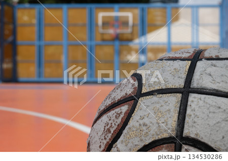 A close-up of a worn basketball's surface contrasts with the background of an outdoor court. A close-up of a worn basketball's surface contrasts with the background of an outdoor court. 134530286