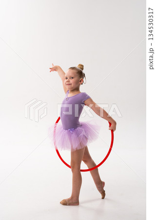 Little ballerina with cochlear implant performing pose with red hoop. Inclusion, hearing awareness, and childhood empowerment through rhythm, color and balance. 134530317