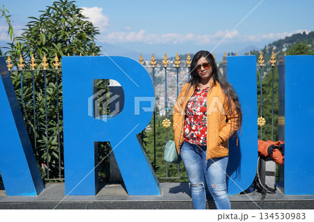 Young beautiful Indian woman posing in front of blue Darjeeling sign board at a scenic hill station viewpoint in West Bengal India 134530983