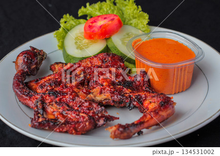 Ayam Taliwang, traditional Lombok spicy grilled chicken dish served on a plate with fresh vegetables and sambal chili sauce. Ayam Taliwang, traditional Lombok spicy grilled chicken dish served on a plate with fresh vegetables and sambal chili sauce. 134531002