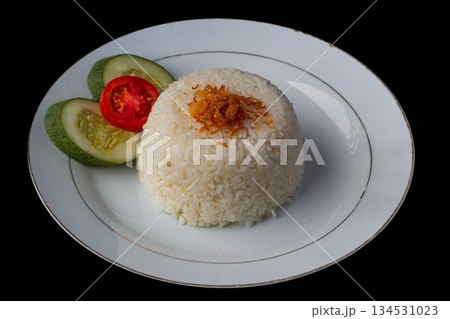 White rice dome topped with fried shallots, served with fresh tomato and cucumber slices on a white plate, isolated on black background. White rice dome topped with fried shallots, served with fresh tomato and cucumber slices on a white plate, isolated on black background. 134531023