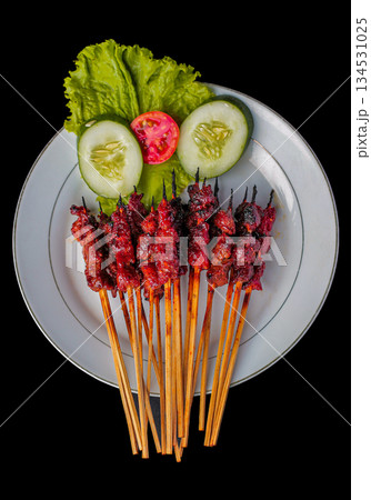 Sate Rembiga, traditional spicy grilled beef skewers from Lombok, Indonesia, served on white plate with fresh salad against black background. Sate Rembiga, traditional spicy grilled beef skewers from Lombok, Indonesia, served on white plate with fresh salad against black background. 134531025