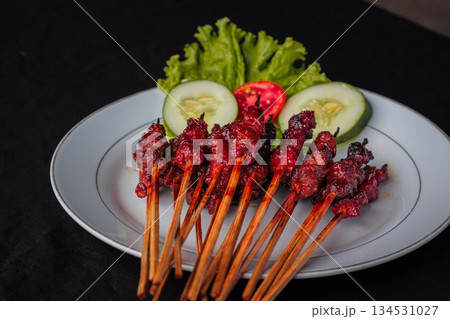Sate Rembiga, traditional spicy skewered beef specialty from Lombok, Indonesia, served on white plate with fresh vegetables. Sate Rembiga, traditional spicy skewered beef specialty from Lombok, Indonesia, served on white plate with fresh vegetables. 134531027