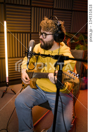 Man vocal artist singing in a recording studio with guitar. Male singer singing a song and playing guitar. Sound record and music streaming concept Man vocal artist singing in a recording studio with guitar. Male singer singing a song and playing guitar. Sound record and music streaming concept 134531618