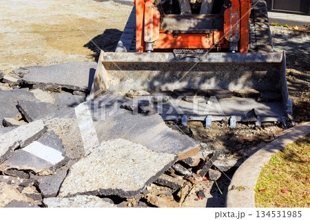 Bulldozer bucket is lifting broken asphalt from construction site, road repair process. 134531985