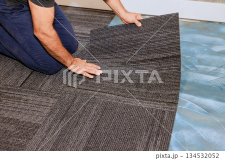 Contractor carefully places black striped carpet tile in stylish office setting under renovation. 134532052