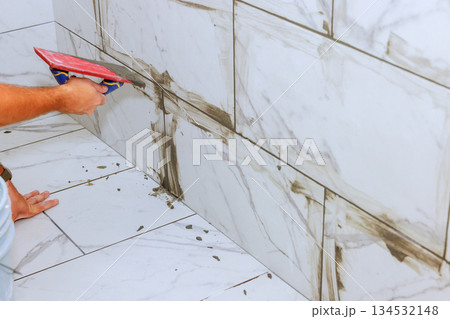 Worker carefully spreads grout between marble tiles in stylish bathroom renovation 134532148