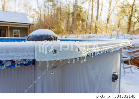 Icicles hang from edge of pool on cold winter day with snow covering ground trees. 134532149