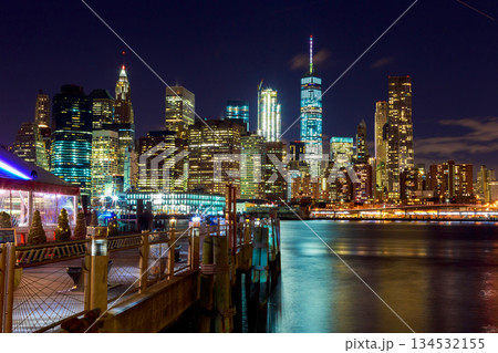 New York city Manhattan skyline at night with buildings lit up reflections in water near dock area. 134532155