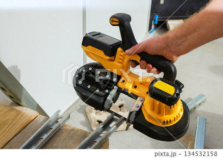 Skilled hands battery operated saw cutting metal framing at workshop 134532158