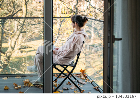 Woman sits on chair on balcony reading book surrounded by fallen autumn leaves. Slow living, urban solitude, mindful moments, simple pleasures. Woman sits on chair on balcony reading book surrounded by fallen autumn leaves. Slow living, urban solitude, mindful moments, simple pleasures. 134532167