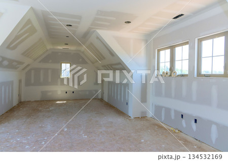 Spacious room with unfinished drywall bare floors, awaiting interior finishing touches in newly built house. 134532169