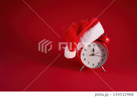Festive Time. A red clock adorned with a Santa hat against a vibrant red background. Festive Time. A red clock adorned with a Santa hat against a vibrant red background. 134532466