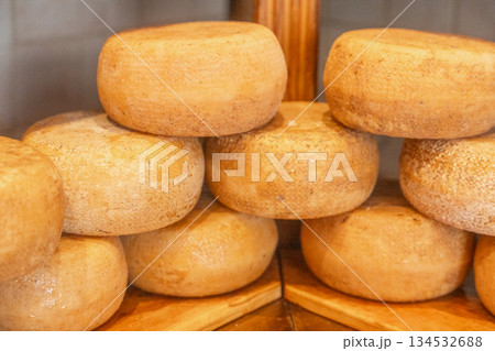 Round cheese wheels stored on wooden shelves in cheese shop. Traditional food storage and artisan production Round cheese wheels stored on wooden shelves in cheese shop. Traditional food storage and artisan production 134532688