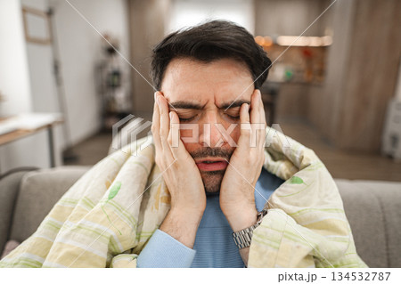 Sick man is sitting covered and has a headache Sick man is sitting covered and has a headache 134532787