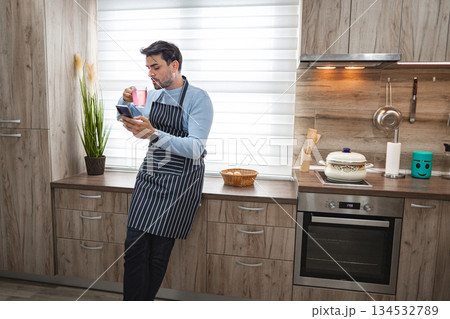 Man in the kitchen using mobile phone while waiting for meal to cook Man in the kitchen using mobile phone while waiting for meal to cook 134532789