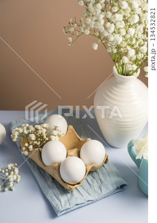 Easter eggs background. White eggs in cardboard box and gypsophila flowers in a vase. Spring holiday 134532821