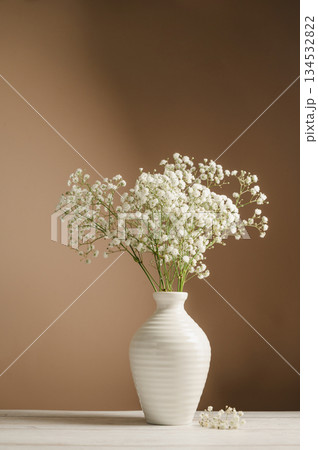 White floral background. Soft home decor, vase with white small flowers on white background, copy space White floral background. Soft home decor, vase with white small flowers on white background, copy space 134532822
