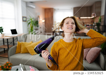Woman Blow Drying Her Hair in Living Room Woman Blow Drying Her Hair in Living Room 134532825