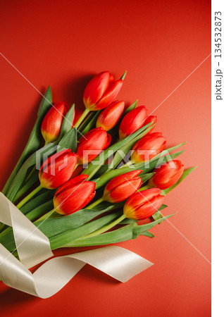 Spring flowers background. A bouquet of fresh red tulips and white ribbon over red background, top view 134532873
